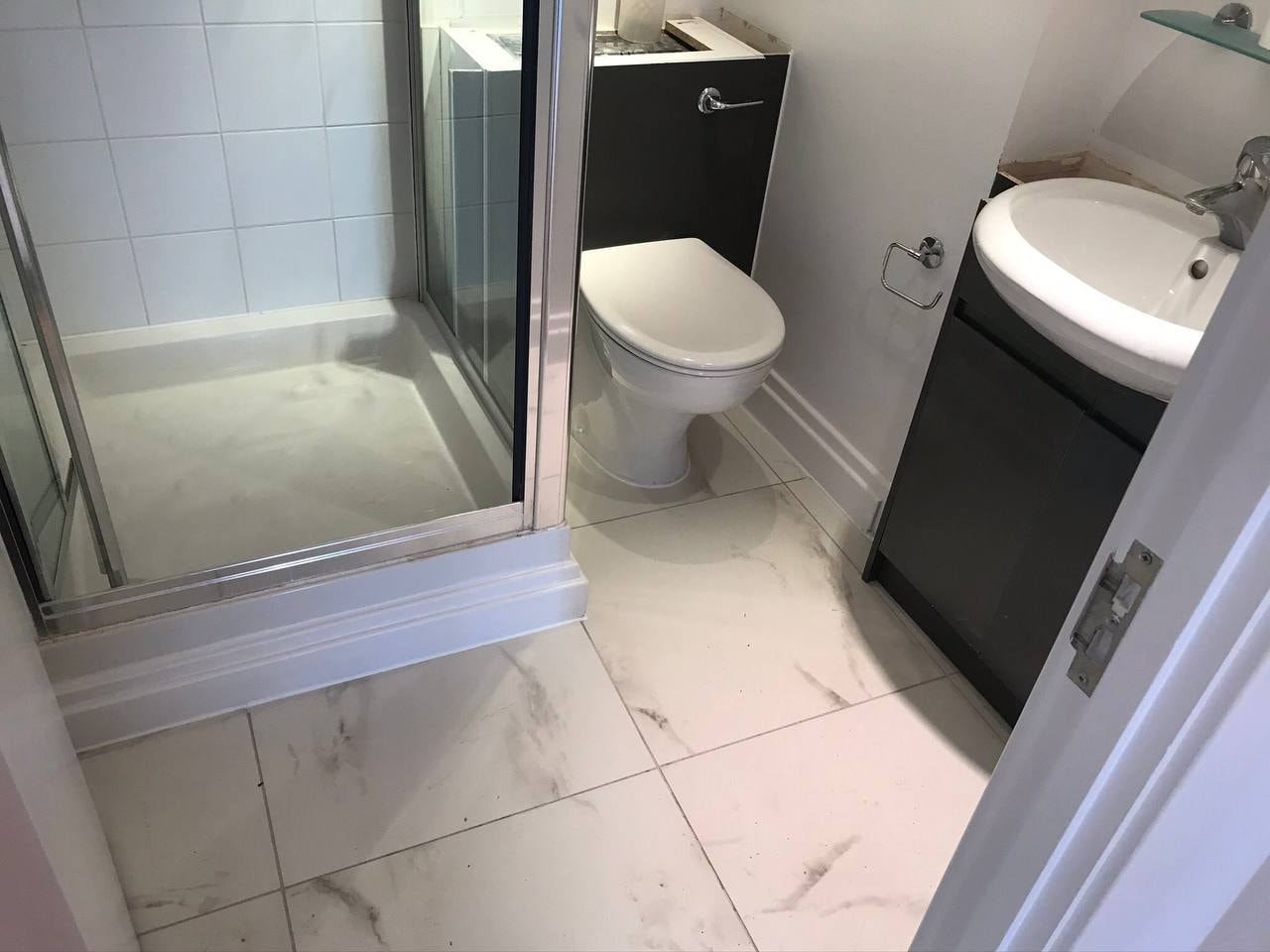 Marble-effect floor tiling in bathroom with dark vanity unit — West London